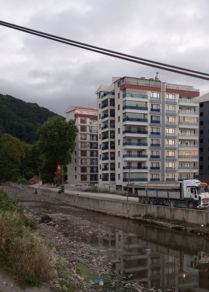 ''Sel felaketlerinin tek nedeni yağışlar değil. Toprağın su tutma kapasitesinin azalması, ormanlık alanların tahrip edilmesi, dere yataklarının daraltılması ve yapılaşmanın bu alanlara kadar genişlemesi, selin yıkıcılığını artırıyor.'' (Çay kenarında yüksek yapılaşmayı gösterir fotoğraf, çalışmanın yazarları tarafından çekilmiştir.)
